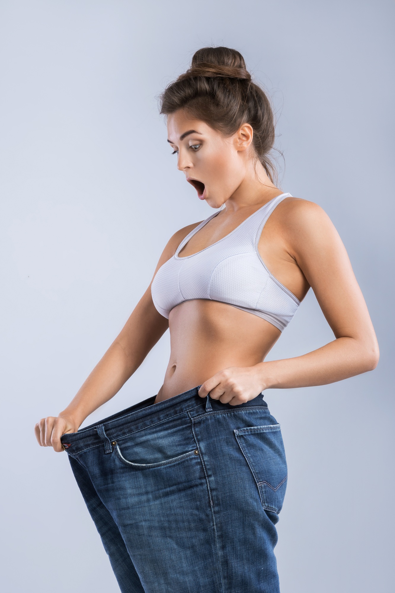 Happy woman wearing jeans after weight-loss on gray background