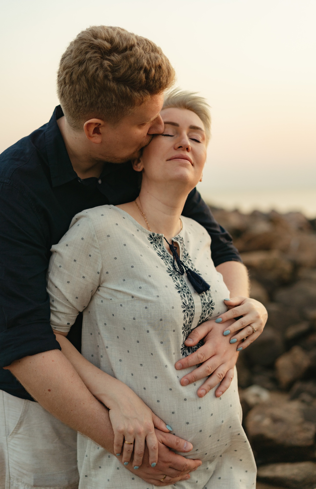 lovely caucaisan couple: man hugging and kissing his pregnant wife by the sea on sunset